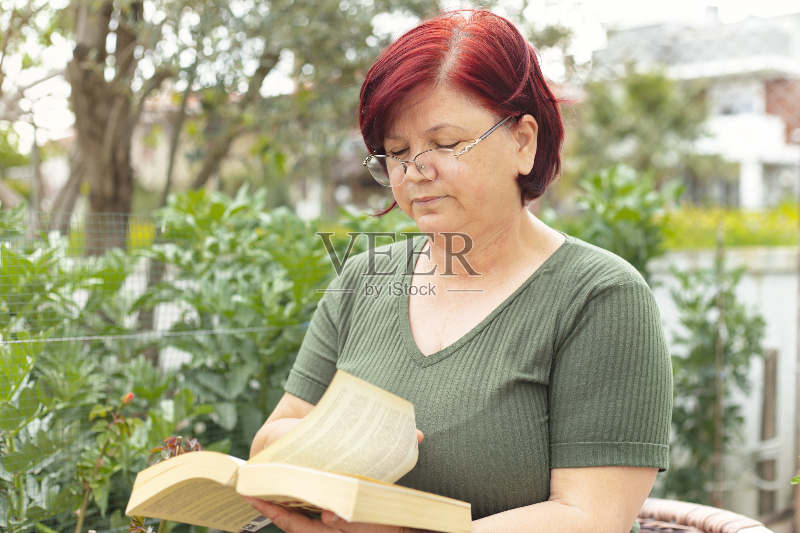 美丽成熟的女人正在她房子的花园里看书。被隔离在家的妇女正在享受一段美好的时光。照片摄影图片