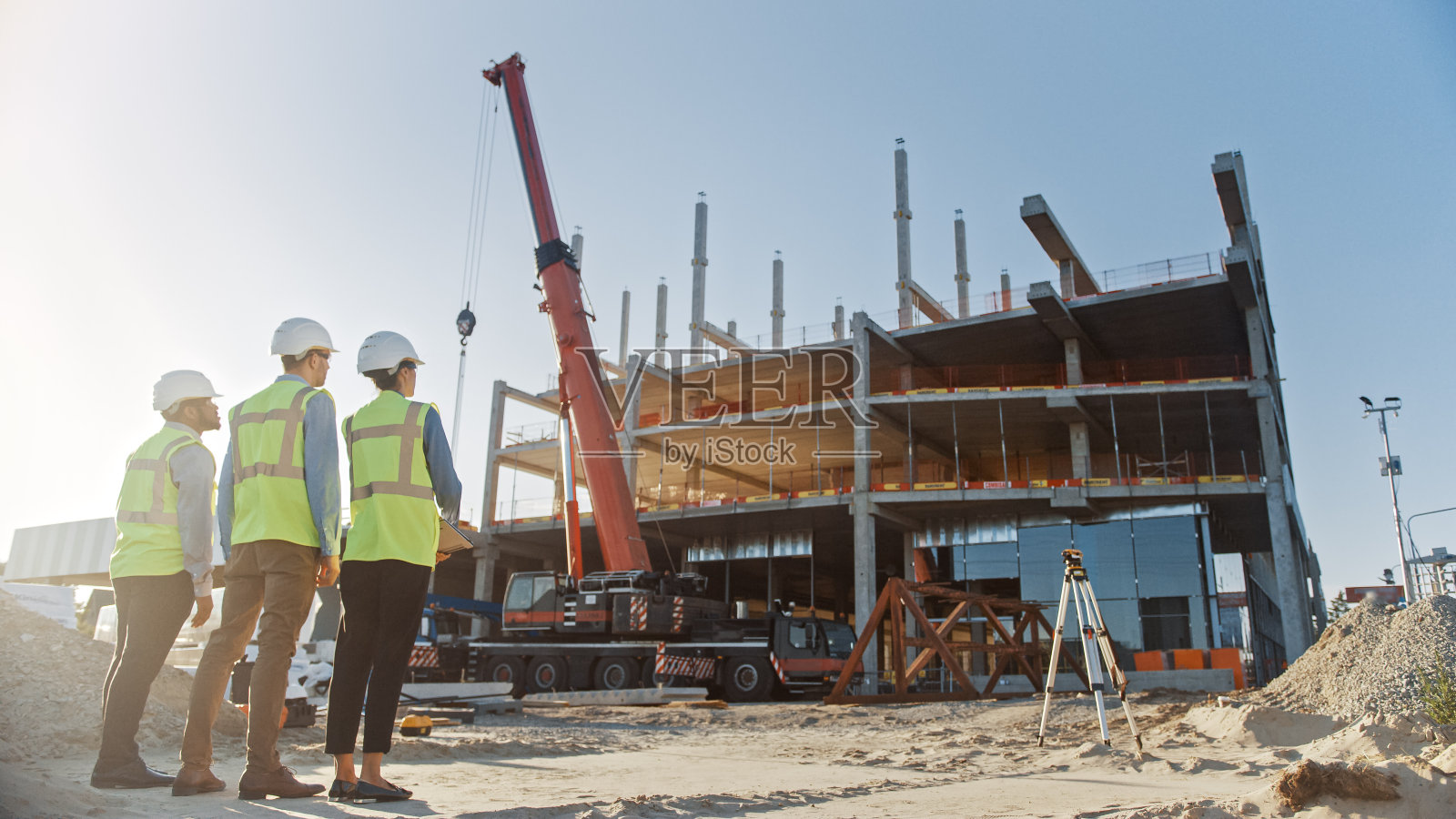 多样化的专家团队检查商业,工业建筑施工现场。房地产项目与土木工程师,投资者和女商人。在背景摩天大楼的模板框架照片摄影图片