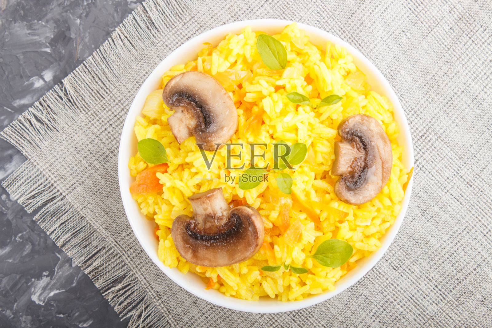 黄色炒饭配香菇,姜黄和牛至,白色陶瓷碗,黑色混凝土背景。俯视图,平躺,特写。照片摄影图片