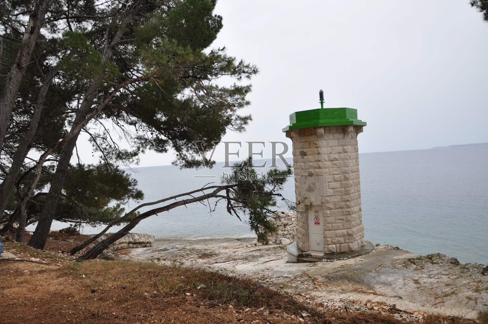灯塔用石头建造,周围是松树和大海照片摄影图片