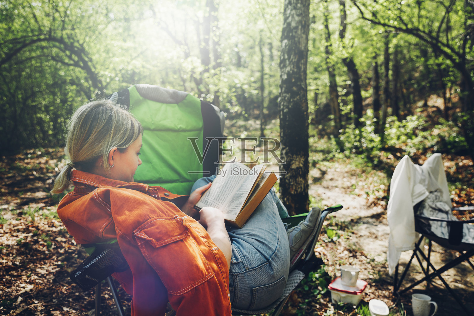 在荒野中寻找孤独的概念。年轻女子在森林里休息,坐在露营椅上看书照片摄影图片
