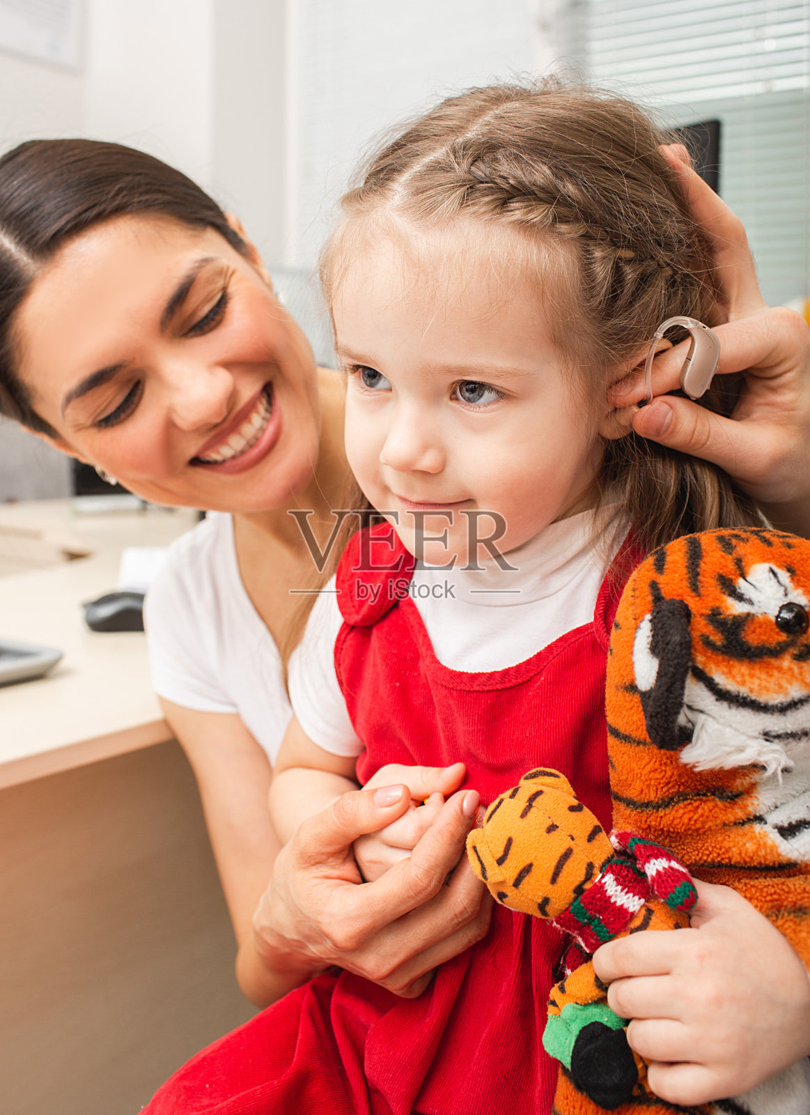 妈妈给女儿看助听器,让她戴着听声音。用助听器治疗耳聋。照片摄影图片