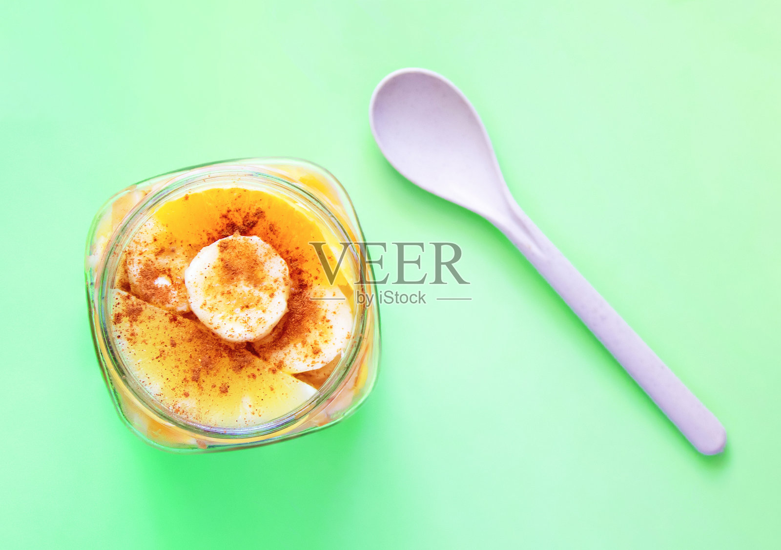 切片水果撒上肉桂,放在一个罐子里,勺子是由天然小麦纤维、淀粉和食品级聚丙烯制成的可生物降解塑料。绿色背景。生态的概念照片摄影图片