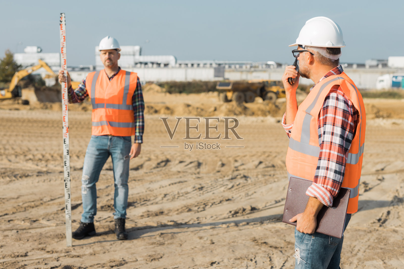 两名身穿橙色背心、头戴钢盔的建筑工在道路施工现场工作照片摄影图片