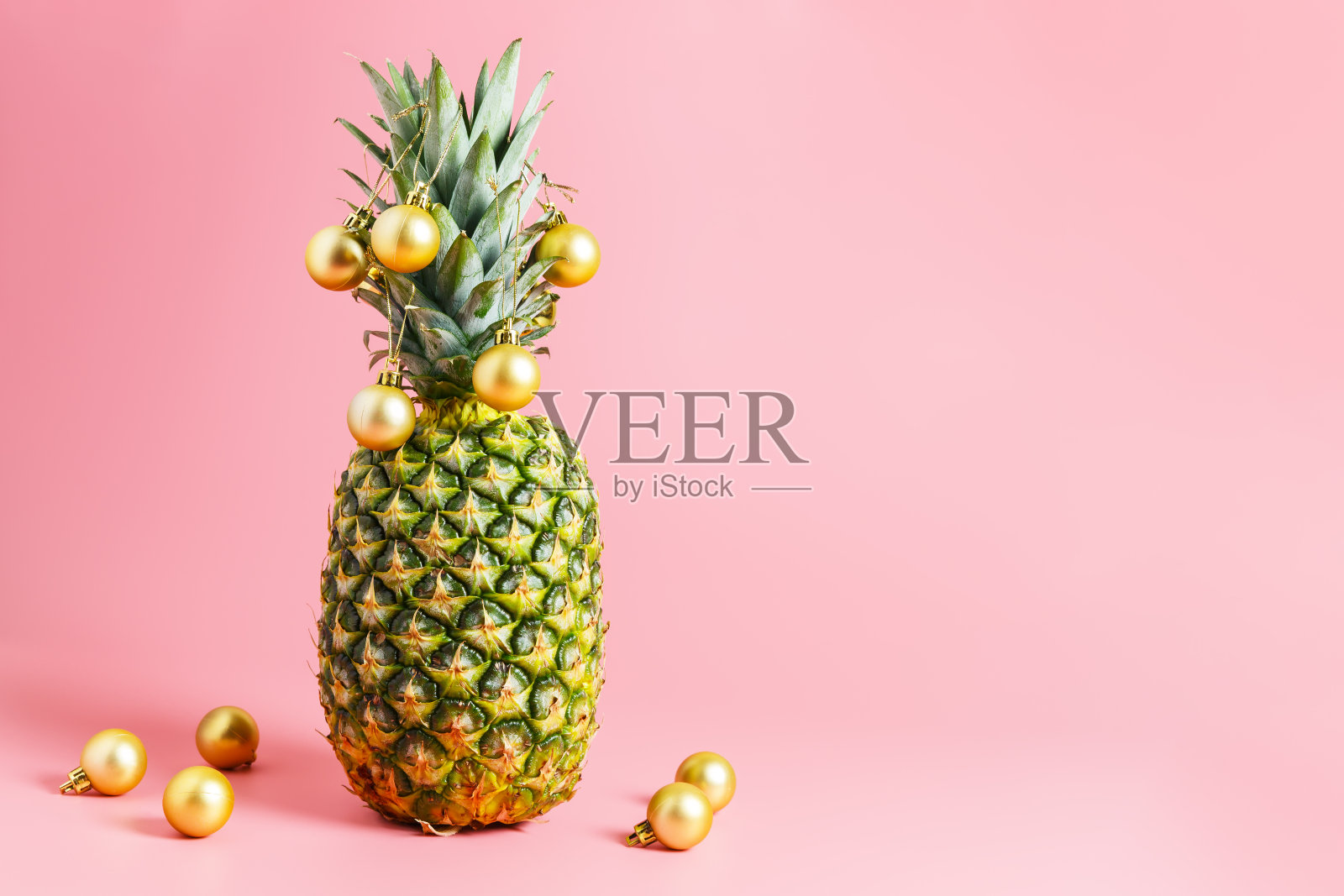 菠萝上的金色圣诞球,粉色背景。菠萝就像圣诞树。照片摄影图片