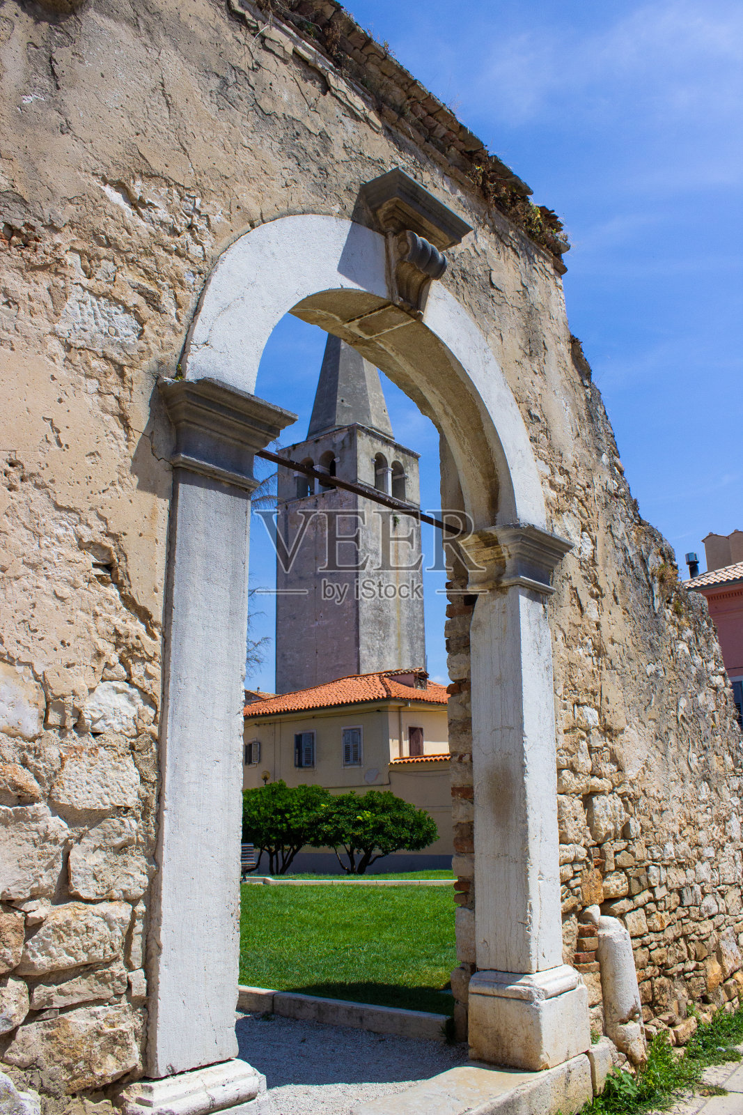 克罗地亚古城Porec(也叫Parenzo)的公园里,一座罗马拱门的遗迹,背景是尤福拉西亚大教堂(也叫圣母升天大教堂)照片摄影图片