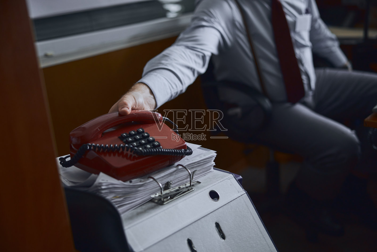 一只手拿着一个低技术含量的按键式手机,放在一堆文件上照片摄影图片