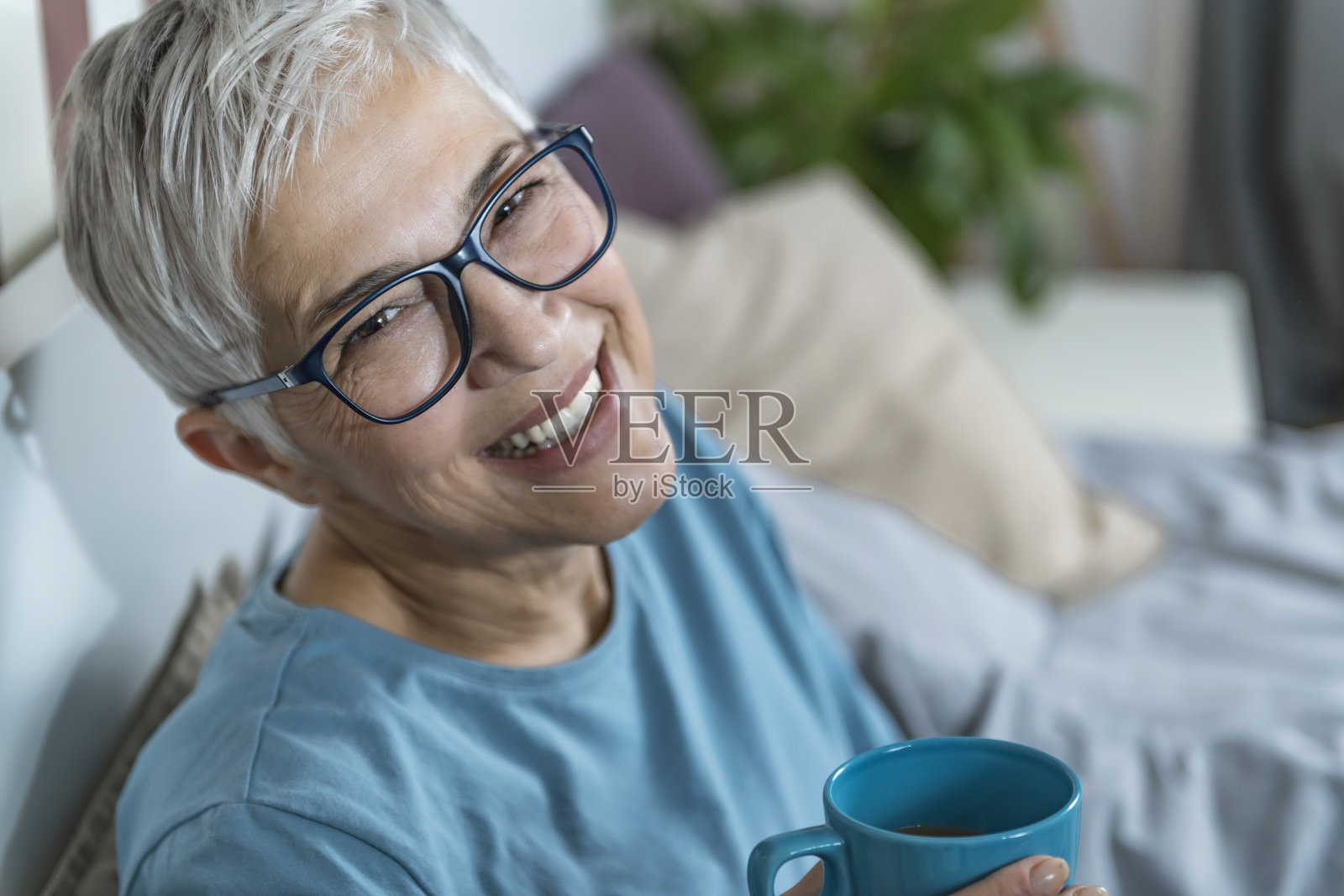微笑的成熟女人躺在床上,喝着咖啡,在睡觉前打电话照片摄影图片
