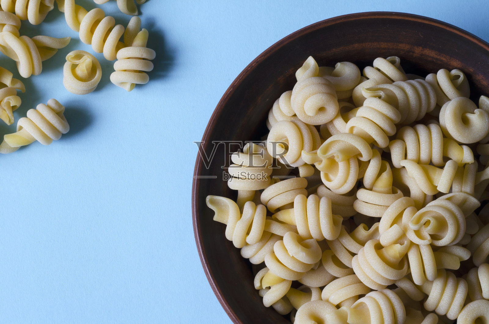 在浅蓝色背景的碗里提供生的沙拉意大利面。照片摄影图片