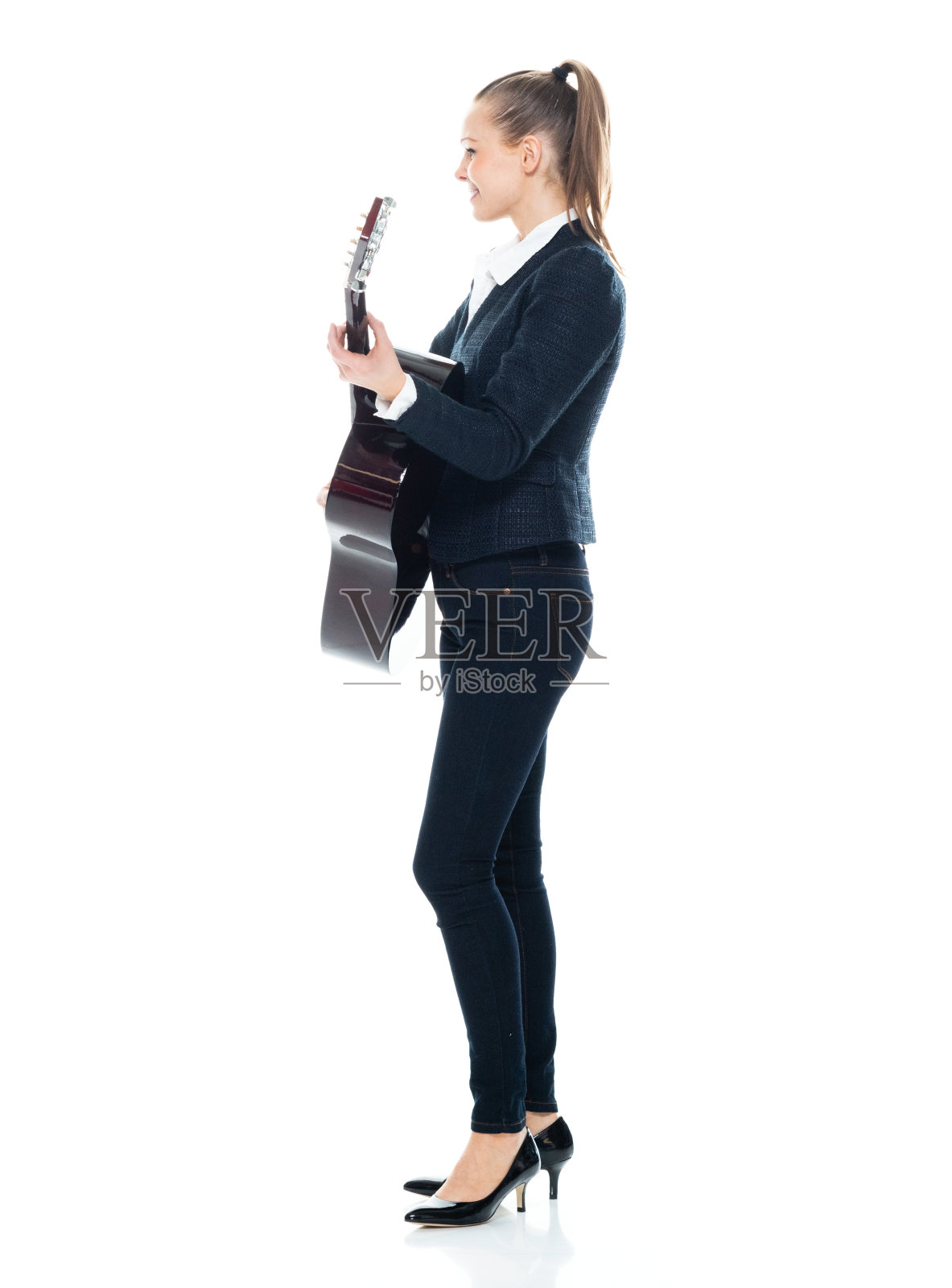 白人年轻女性吉他手站在白色背景穿着牛仔裤和拿着吉他照片摄影图片