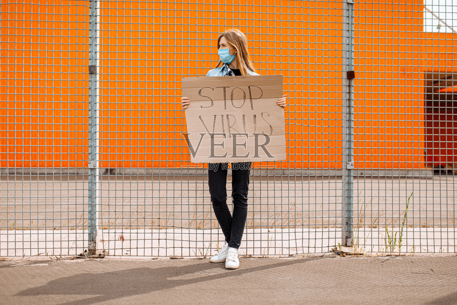 一位戴着医用防护口罩的妇女,拿着一张写着“阻止病毒”的纸板,靠在一堵黄色的墙上照片摄影图片