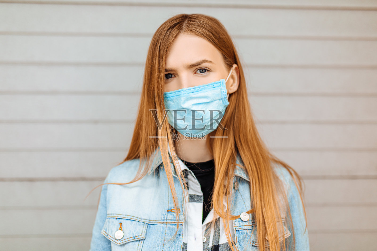 一个戴医用防护面具的女人,靠在一堵灰色的墙上照片摄影图片