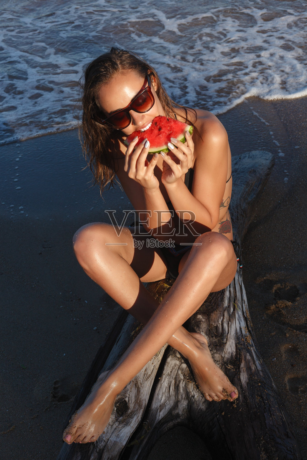 暑假——年轻女孩在沙滩上吃新鲜的西瓜照片摄影图片