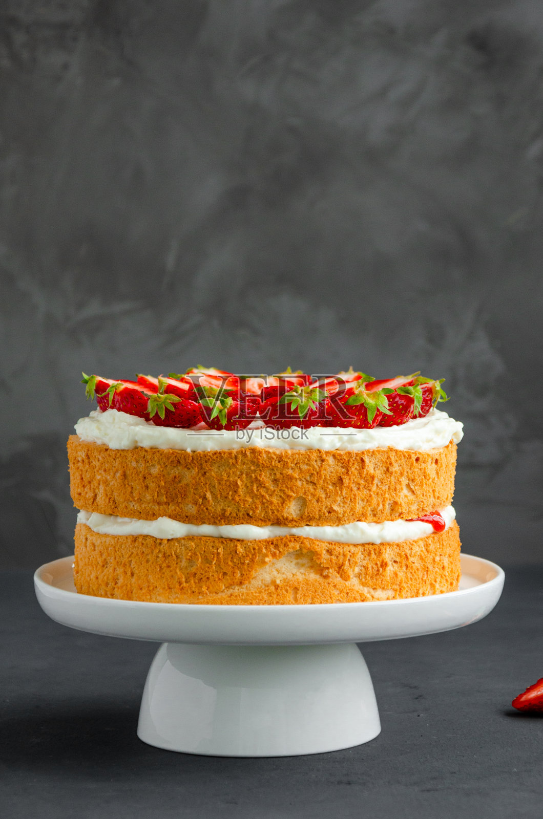 维多利亚海绵蛋糕,草莓酱,鲜奶油和新鲜草莓放在白色的盘子上,灰色的混凝土背景。垂直方向,复制空间。照片摄影图片