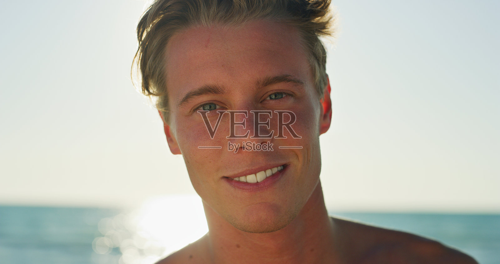 一个微笑的年轻男子的肖像是快乐的享受一个暑假在一个阳光明媚的日子在海边海边。照片摄影图片