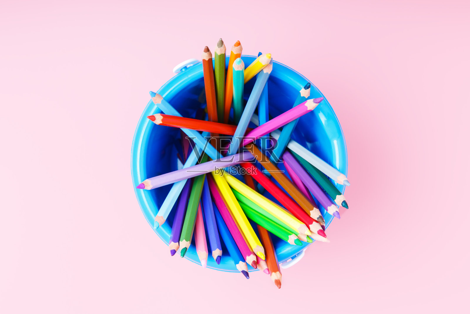 粉红色背景上的蓝色笔筒里的彩色铅笔。照片摄影图片