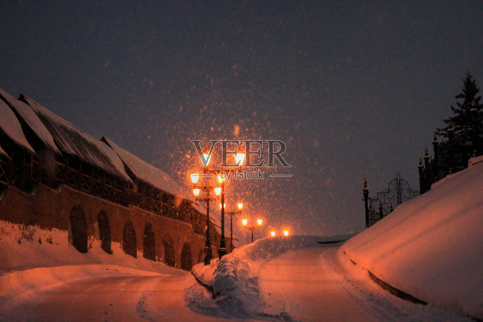 冬天的路和路灯,夜晚的风景。空中飘着很多雪花。左边是古建筑墙。照片摄影图片