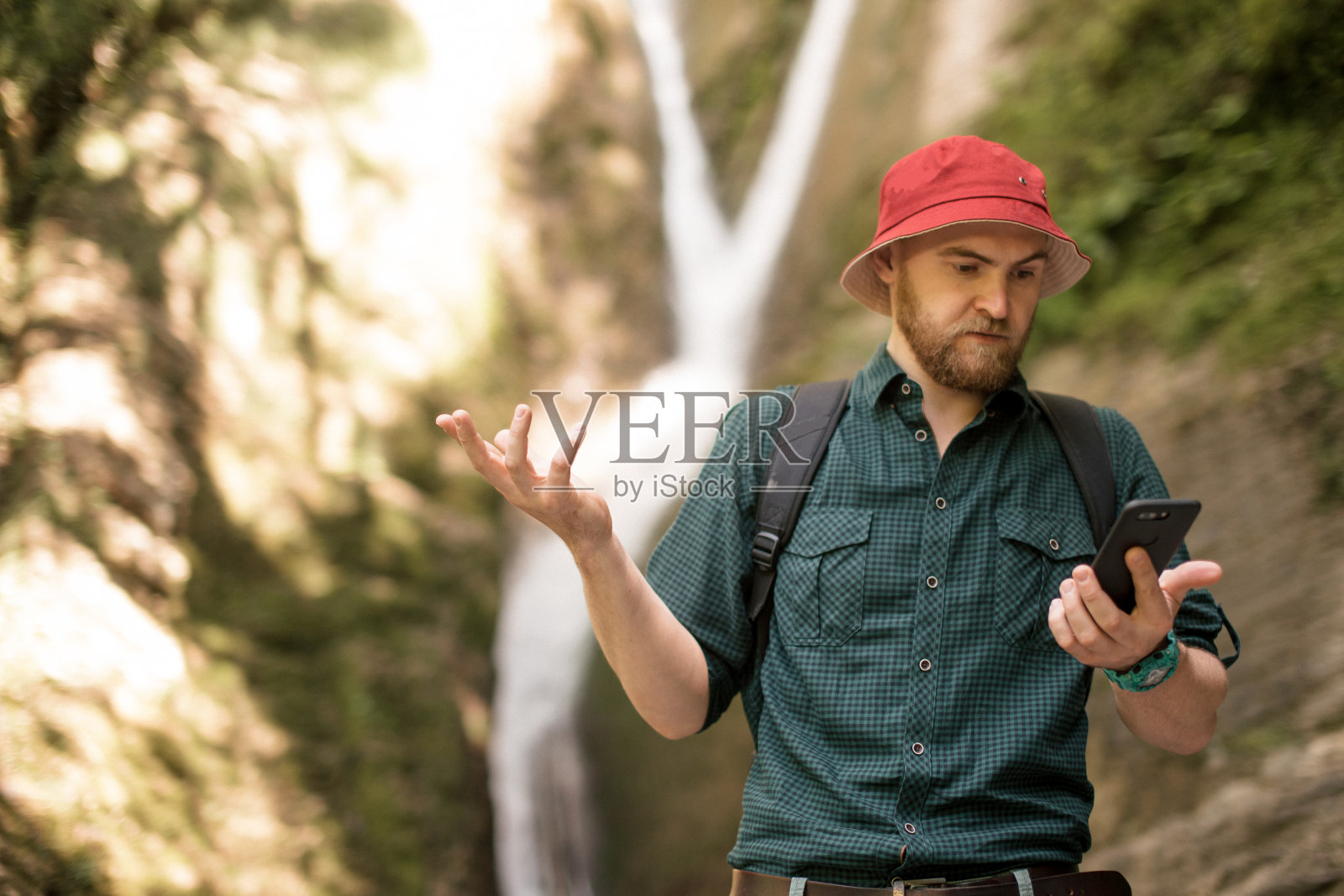 徒步者拿着智能手机试图在森林深处找到瀑布之间的联系。照片摄影图片