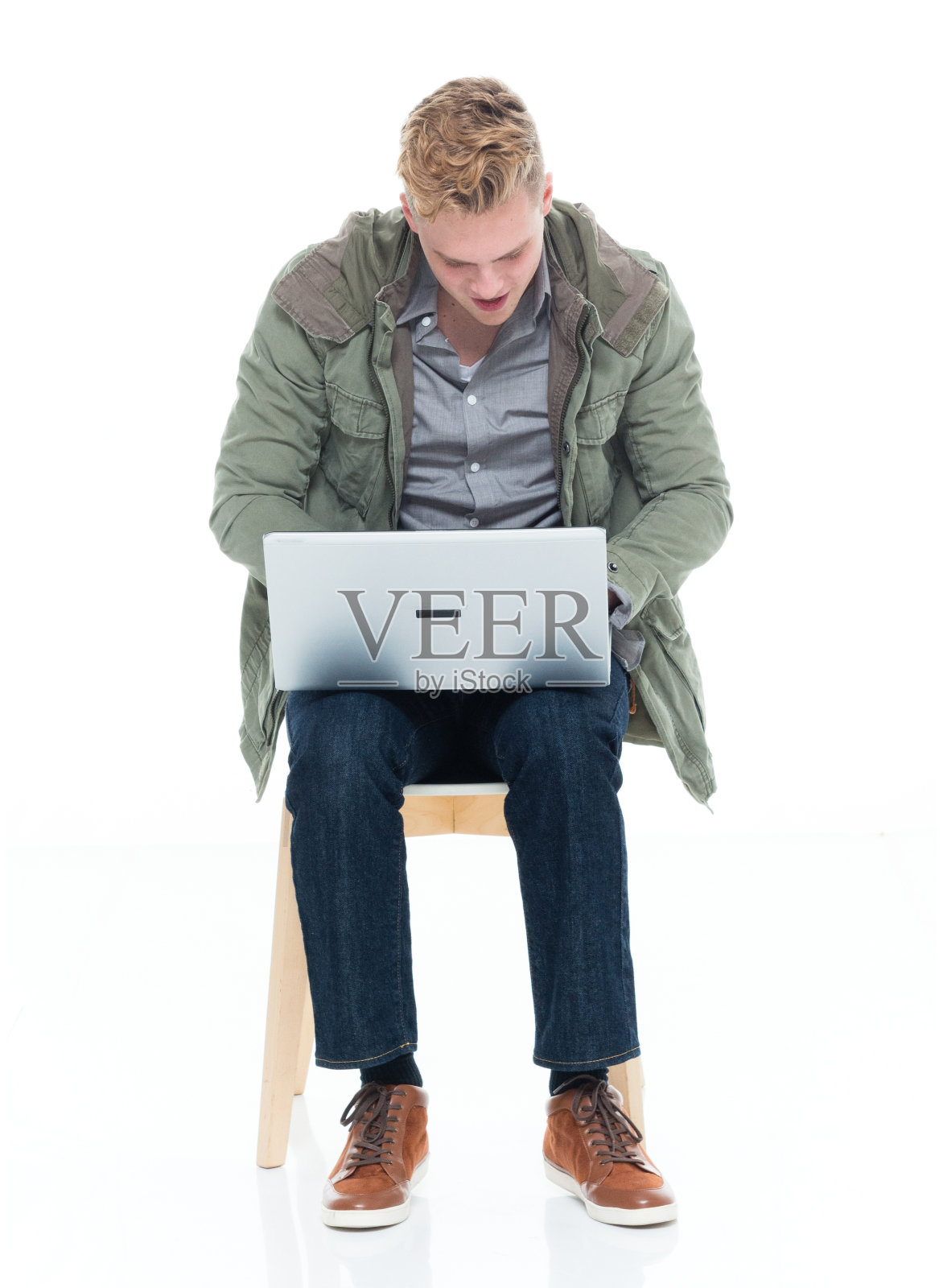 白人男性穿着夹克坐在白色背景前使用笔记本电脑照片摄影图片