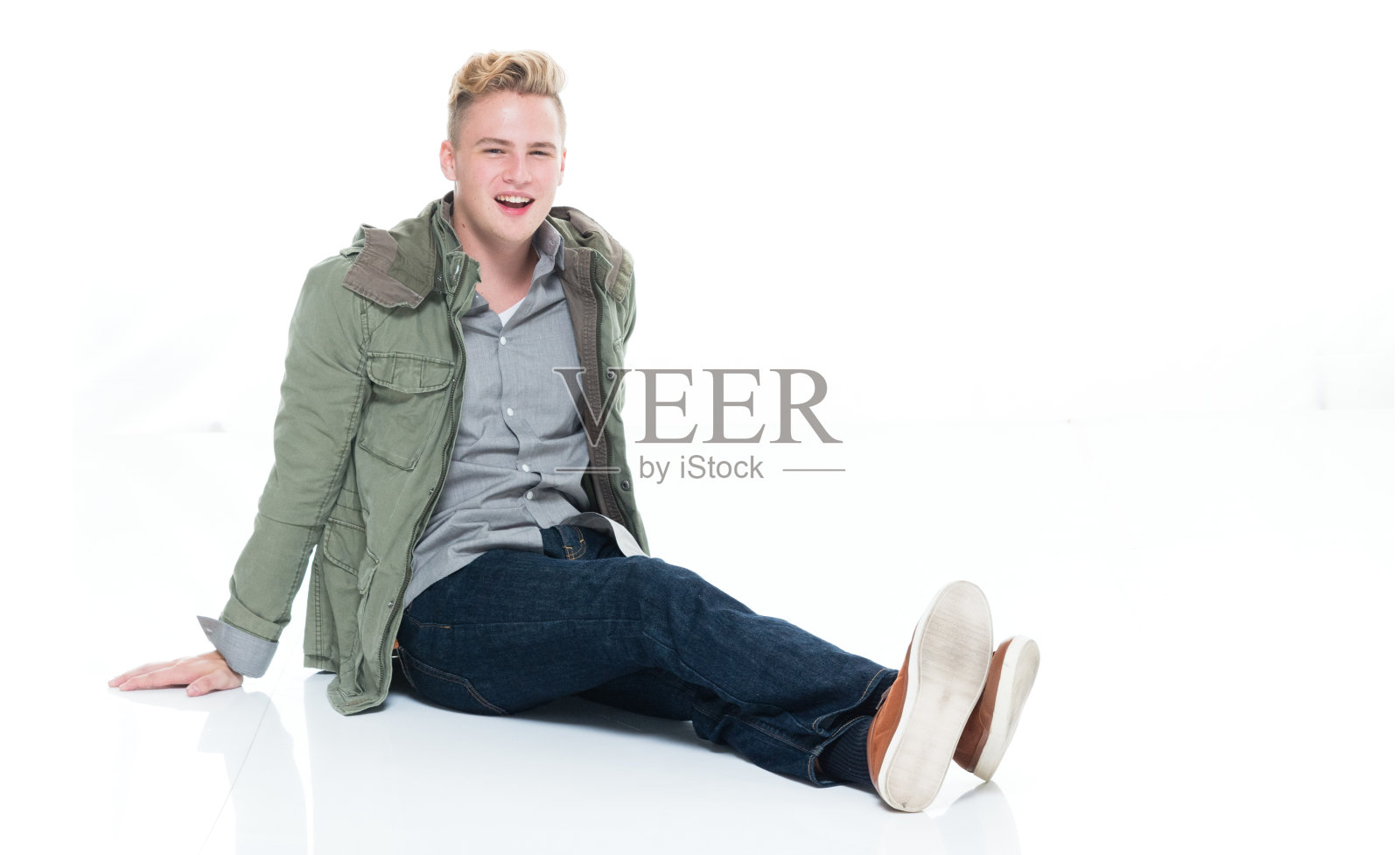 白人十几岁的男孩坐在地板上的白色背景,穿着暖和的衣服照片摄影图片