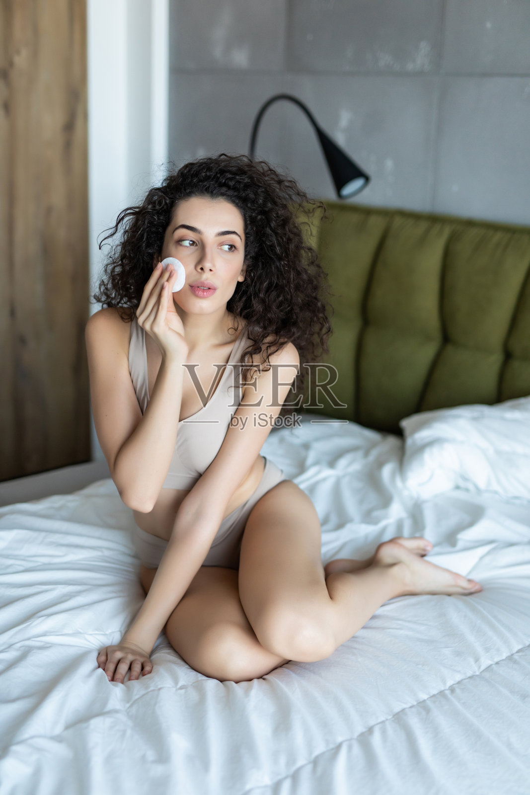 年轻漂亮的女人坐在床上,用棉花海绵擦脸照片摄影图片