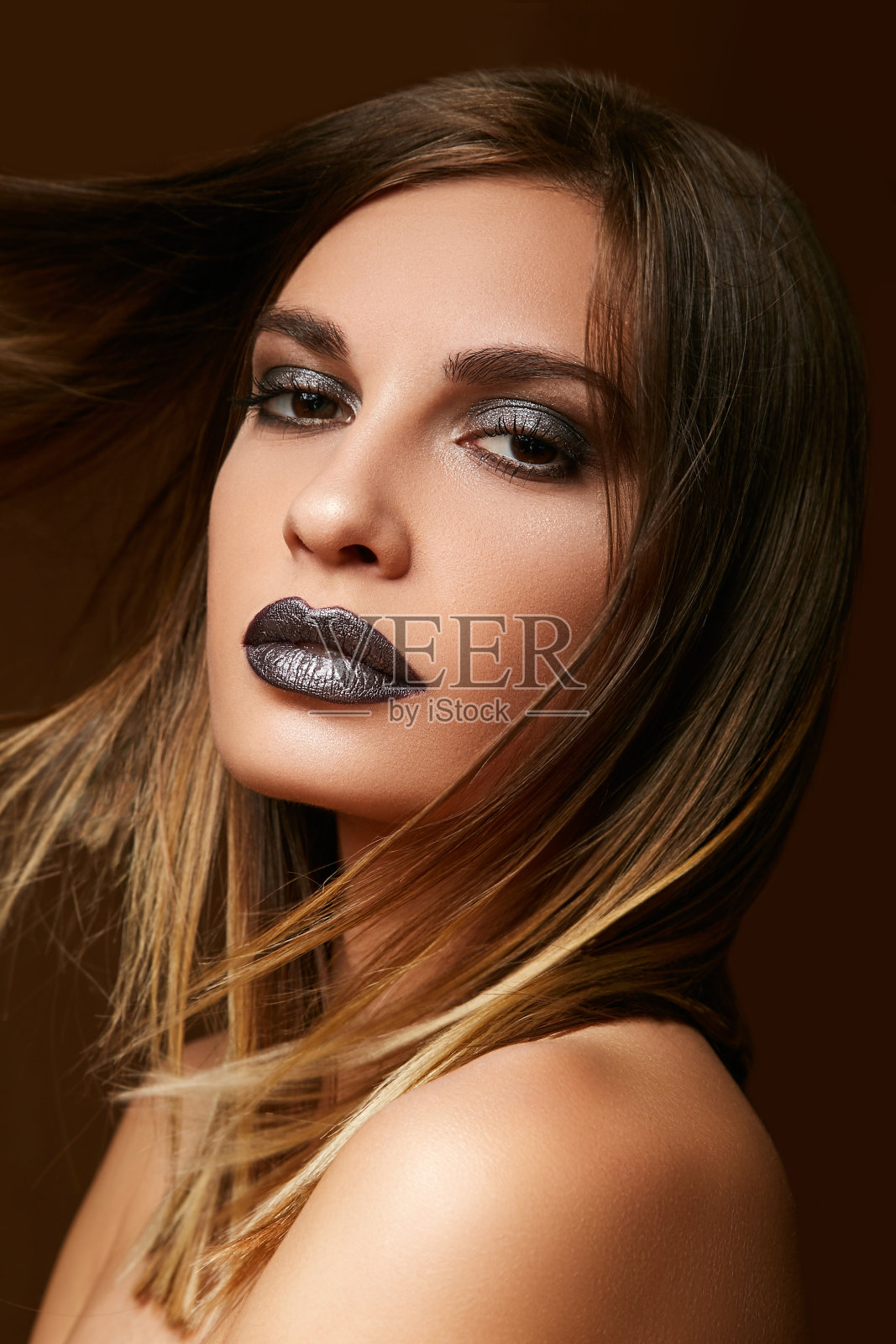 可爱的年轻女孩与黑妆在她的脸近距离摆姿势在一个棕色的背景。照片摄影图片