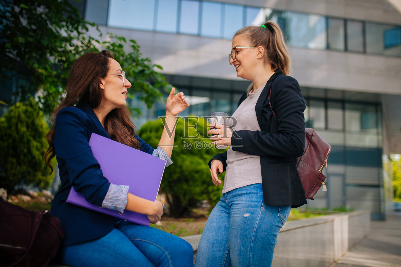 年轻漂亮的女商人在室外谈话。办公楼背景。照片摄影图片