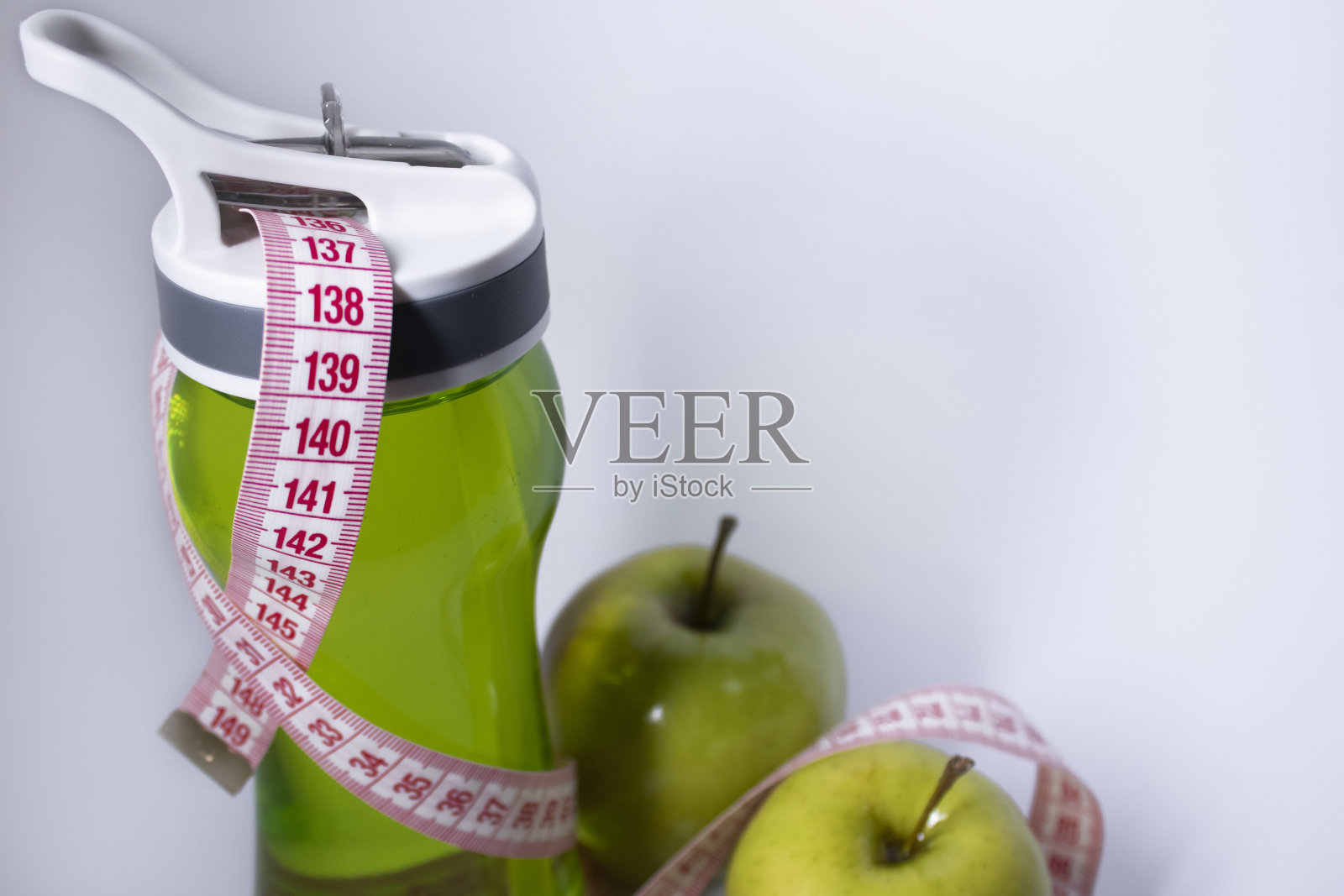 红色卷尺盖住绿色运动瓶和绿色苹果。饮食与健康生活、减肥、运动理念。前视图。副本的空间。孤立。白色背景照片摄影图片