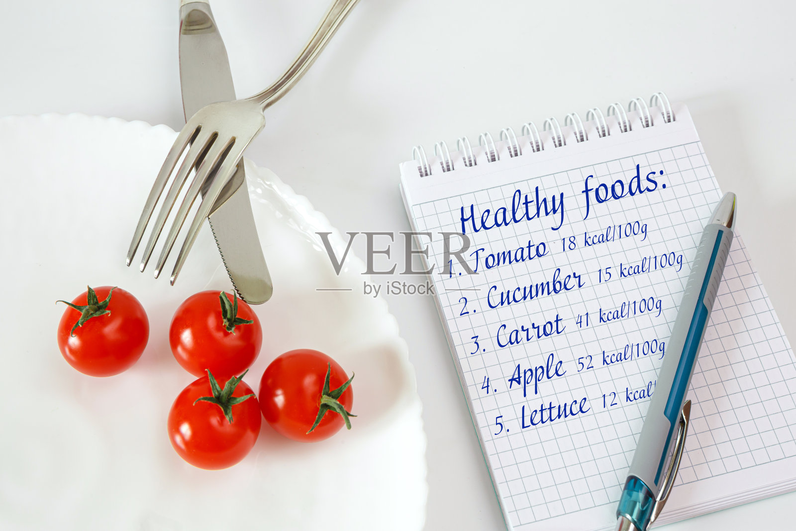 奇瑞番茄放在盘子里,配上刀叉和笔记本照片摄影图片