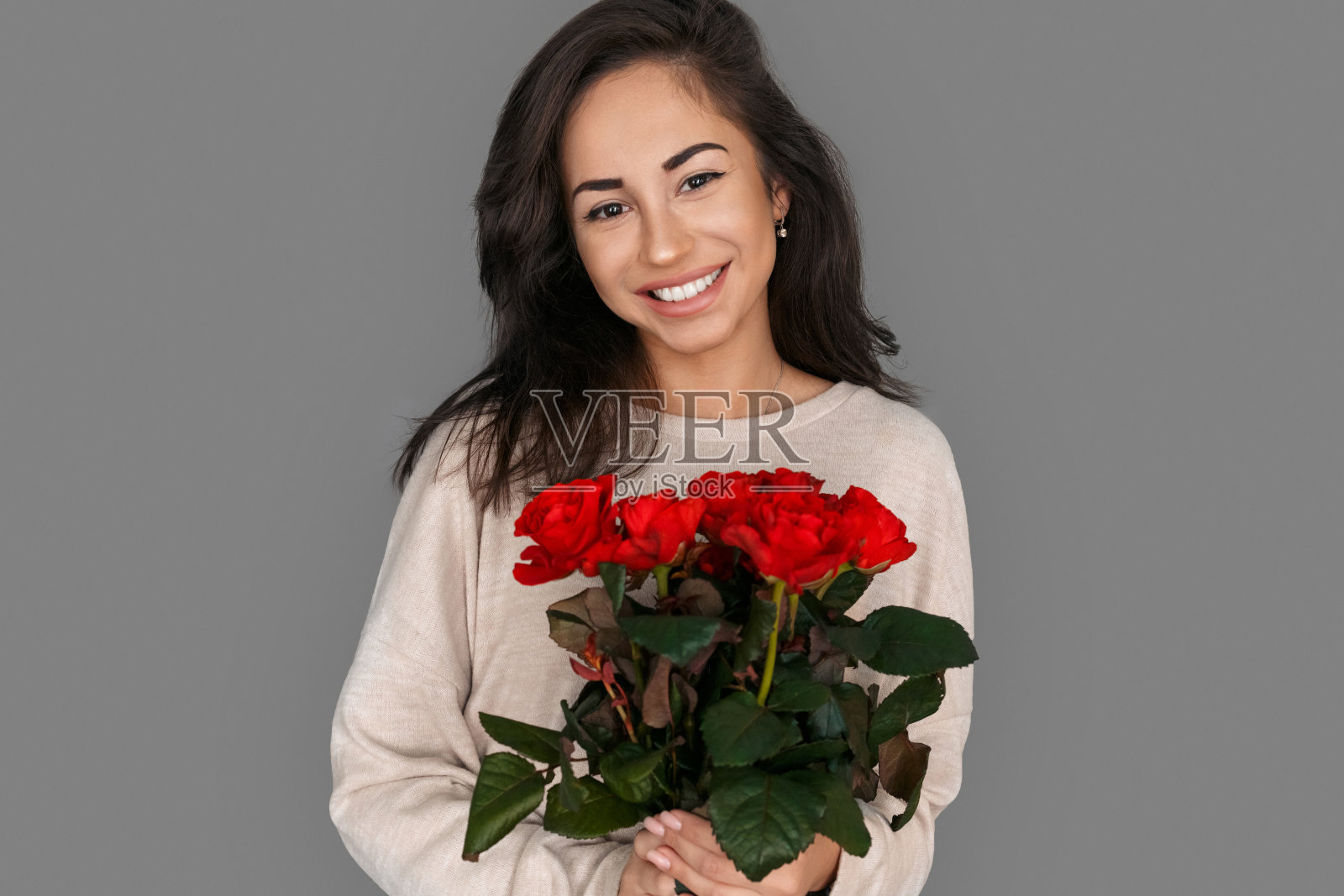 浪漫的礼物。女人孤立地站在灰色的玫瑰花束上,笑容可掬照片摄影图片