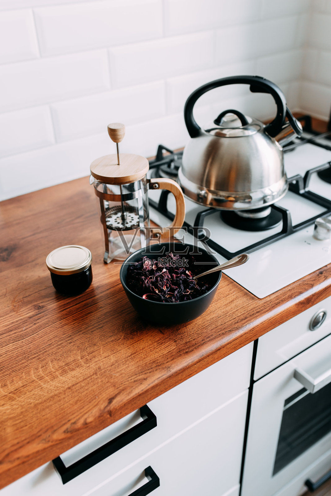 松木槿茶在黑色的碗和勺子,法式榨汁机和蜂蜜罐在木桌上。煤气炉上的金属茶壶。木制完整的厨房与煤气炉。照片摄影图片