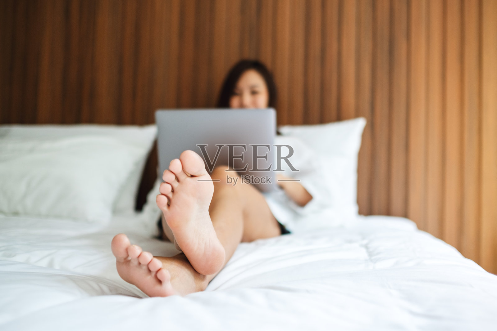 躺在舒适的白色床上用笔记本电脑工作的女人照片摄影图片