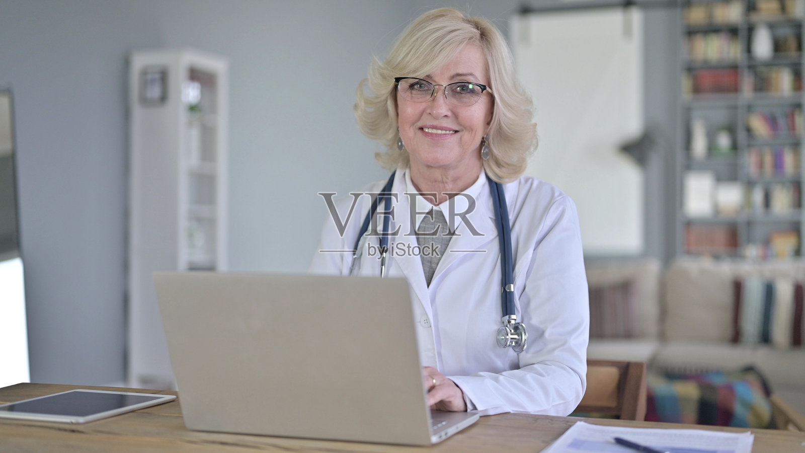 老女医生用笔记本电脑和对着相机微笑照片摄影图片