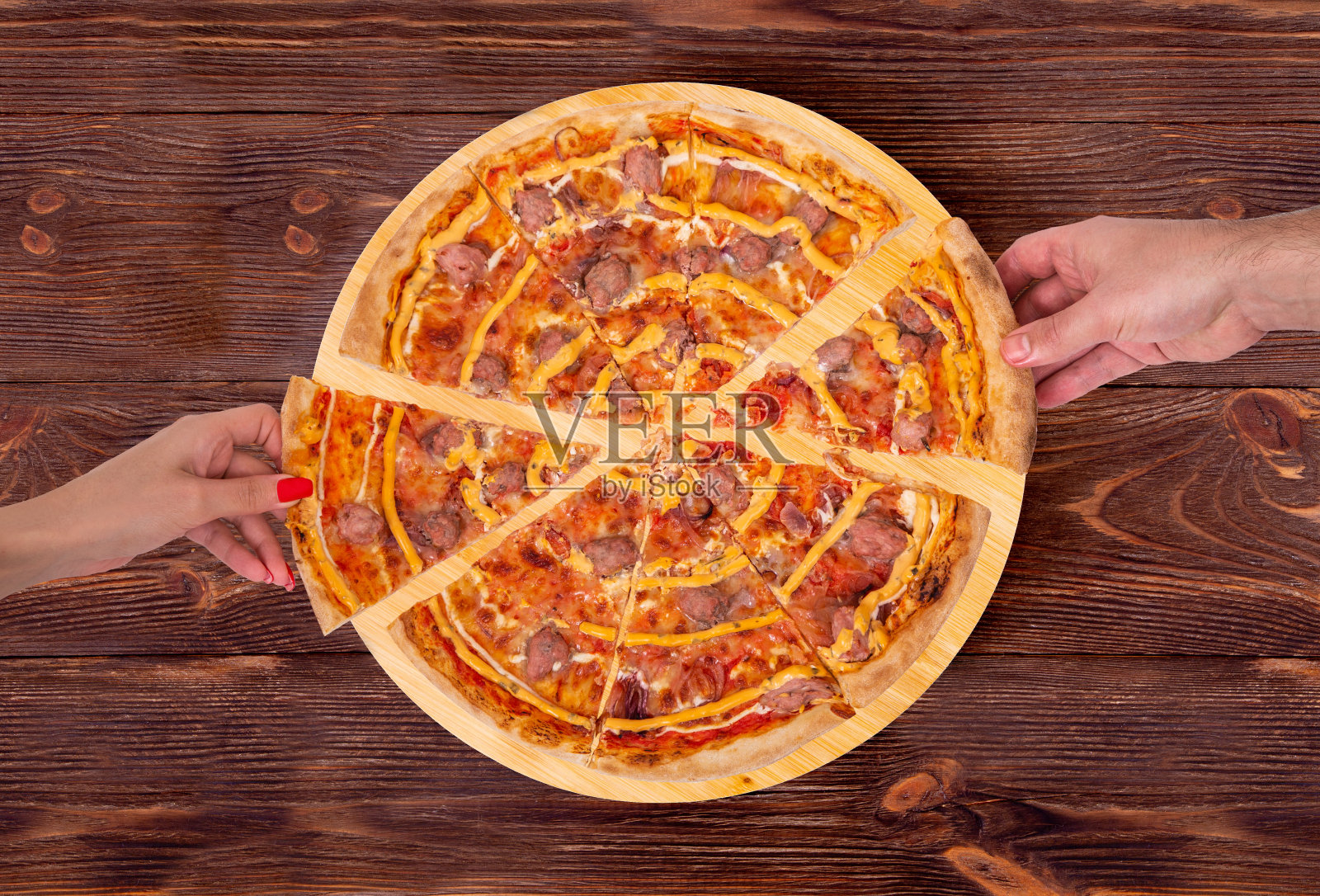 手从木桌上的木盘子里拿起美味的披萨,上面有牛肉香肠、马苏里拉奶酪、各种酱汁和腌制过的红洋葱照片摄影图片
