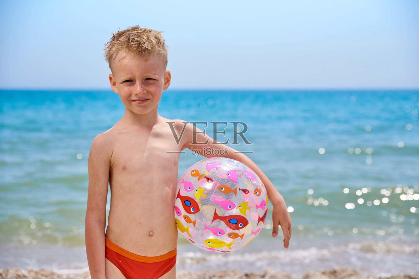 7岁的小男孩带着充气球在海边的沙滩上玩照片摄影图片