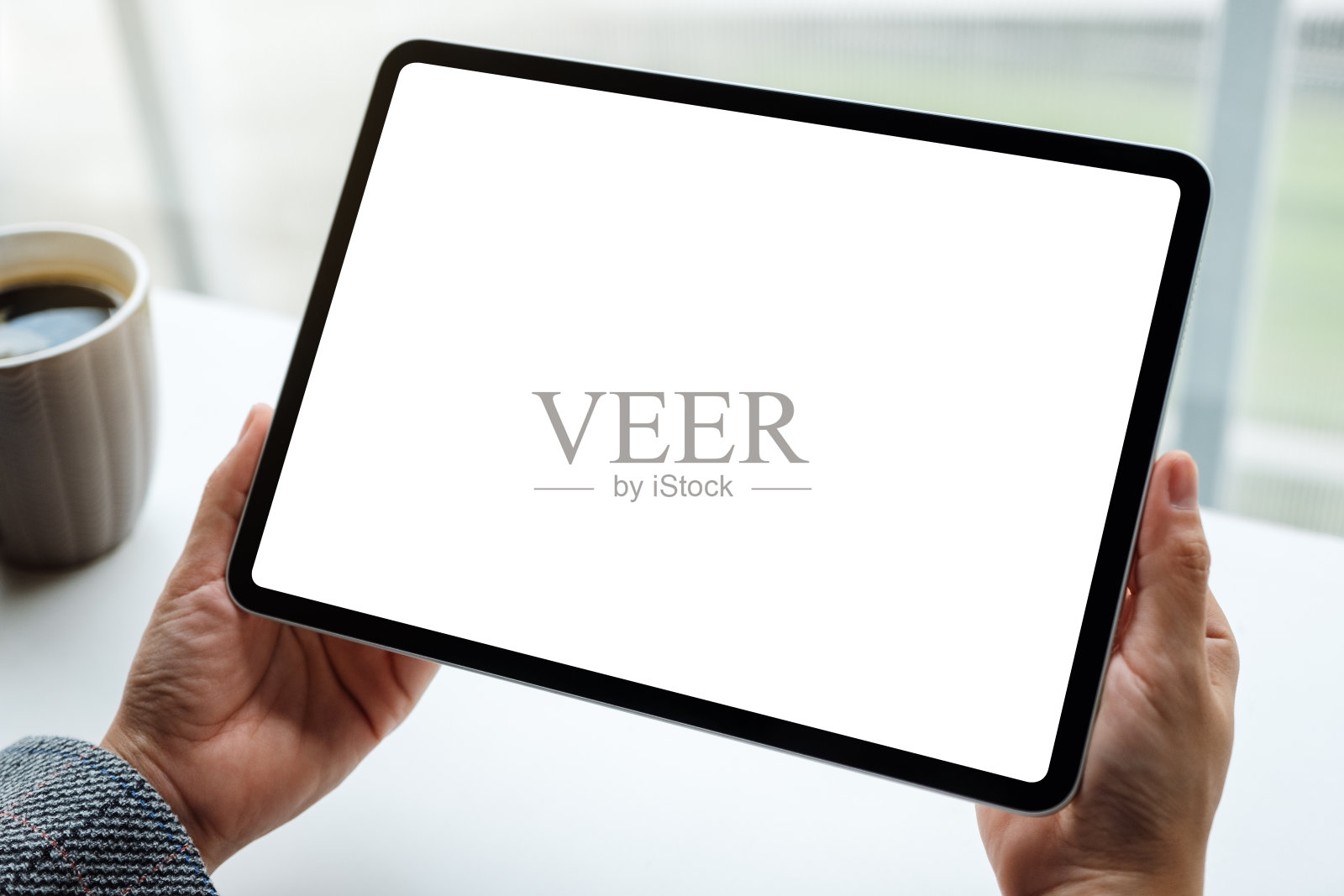 一个女人拿着黑色的平板电脑与空白的白色屏幕和咖啡杯在桌子上照片摄影图片