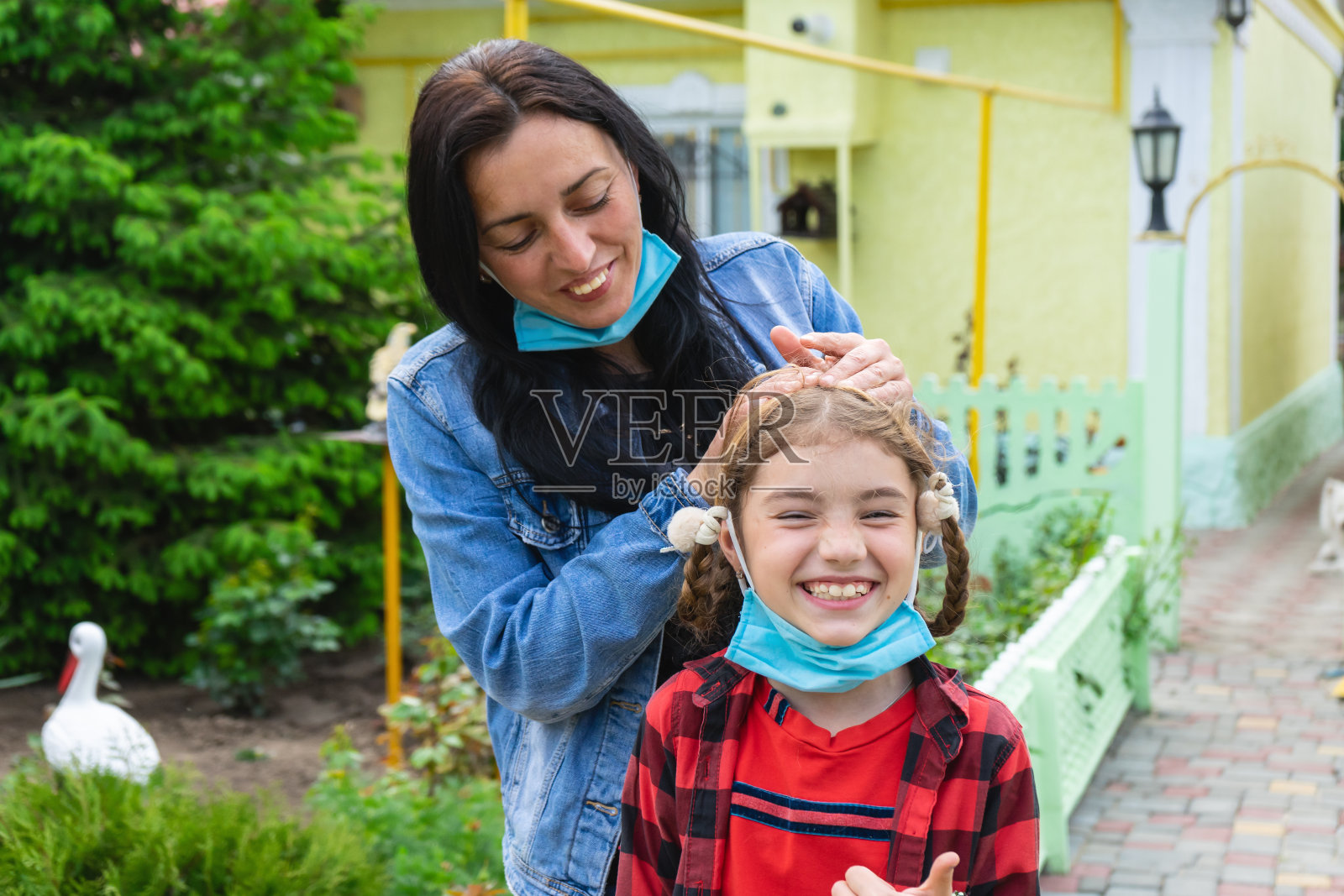 女人和小女孩的肖像戴着面具看着我们,开心地玩。家庭隔离。母亲拥抱着她的小女孩。呆在家里照片摄影图片