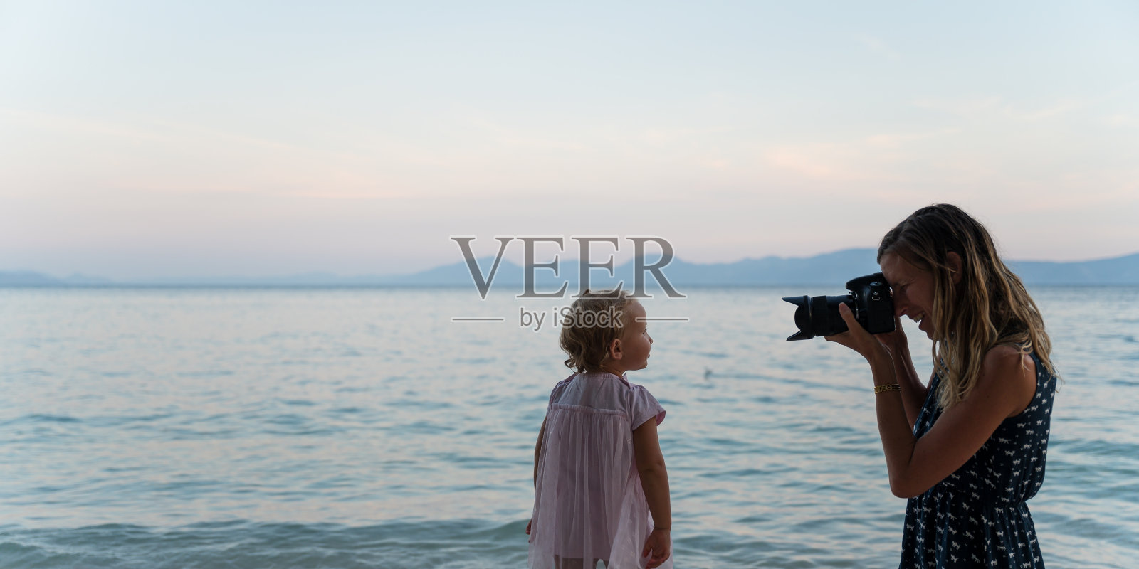 黄昏时分,母亲在海边给女儿拍照照片摄影图片