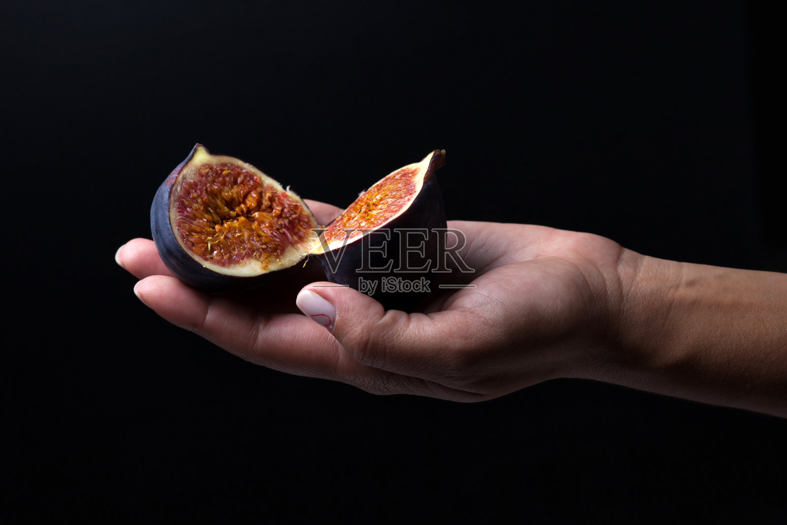无花果躺在一只雌性的手掌上,在黑色的背景。无花果被切成相等的两部分。照片摄影图片