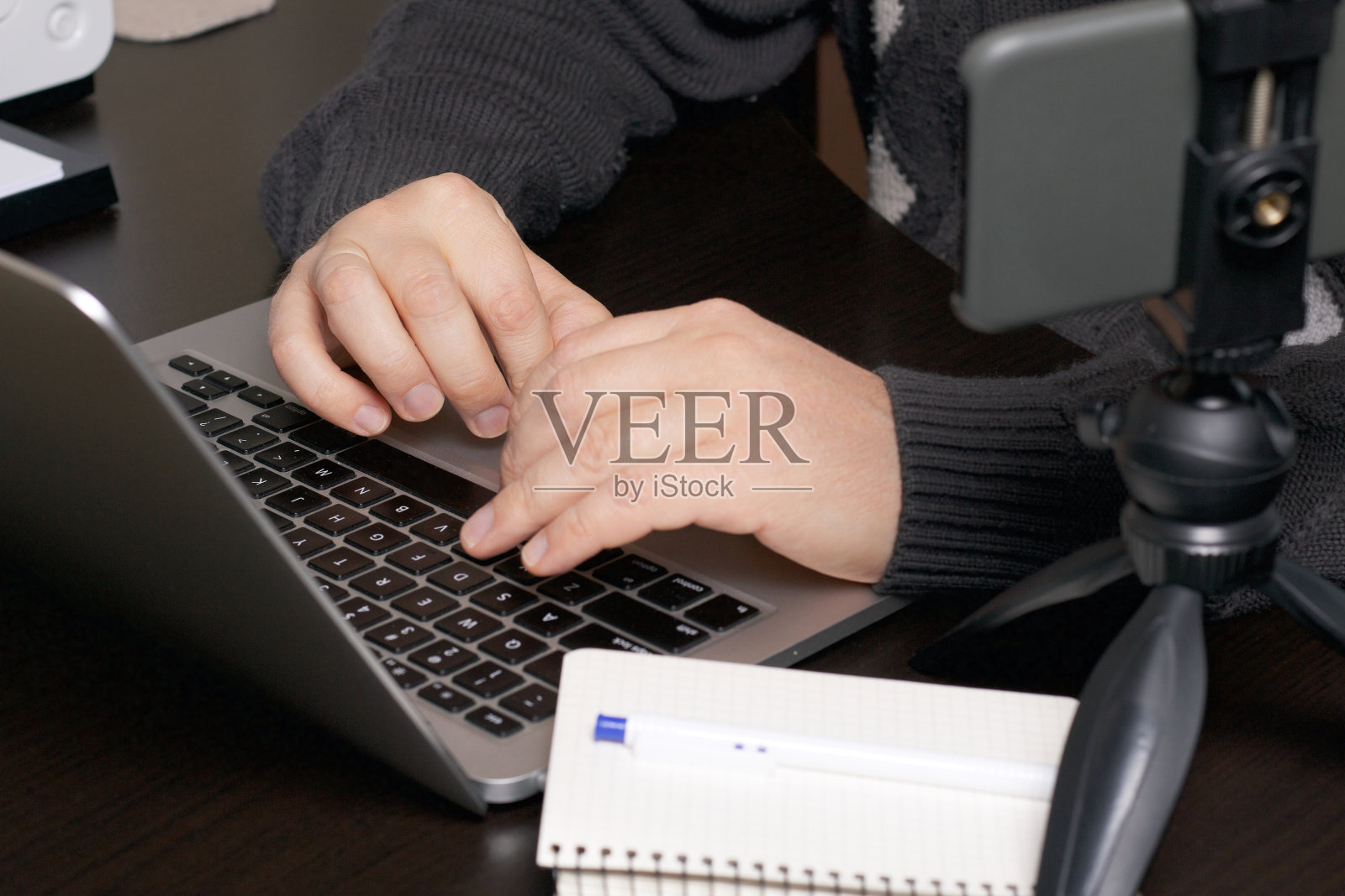 一个男人在笔记本电脑前工作。靠近智能手机的三脚架上,笔记本和笔。双手收得很近。照片摄影图片