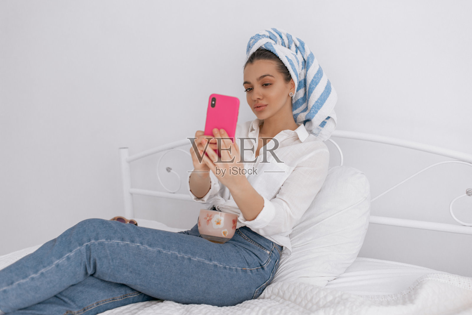 可爱的漂亮女孩戴着毛巾在她的头冷却在家里与电话和一杯茶。美容和化妆品的概念。照片摄影图片