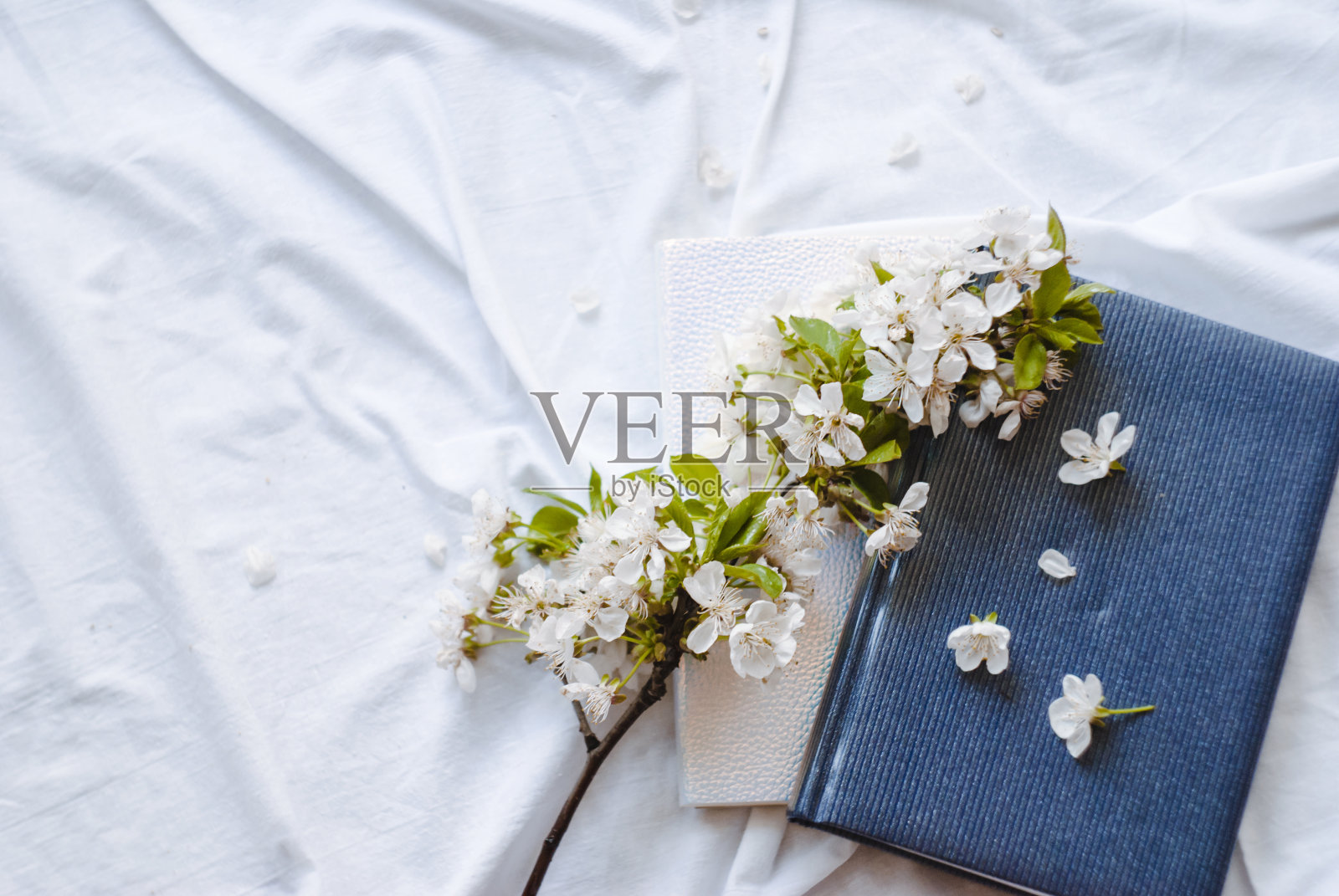 一张白色床上的蓝色笔记本和开花的树枝的特写。文本。平的。照片摄影图片