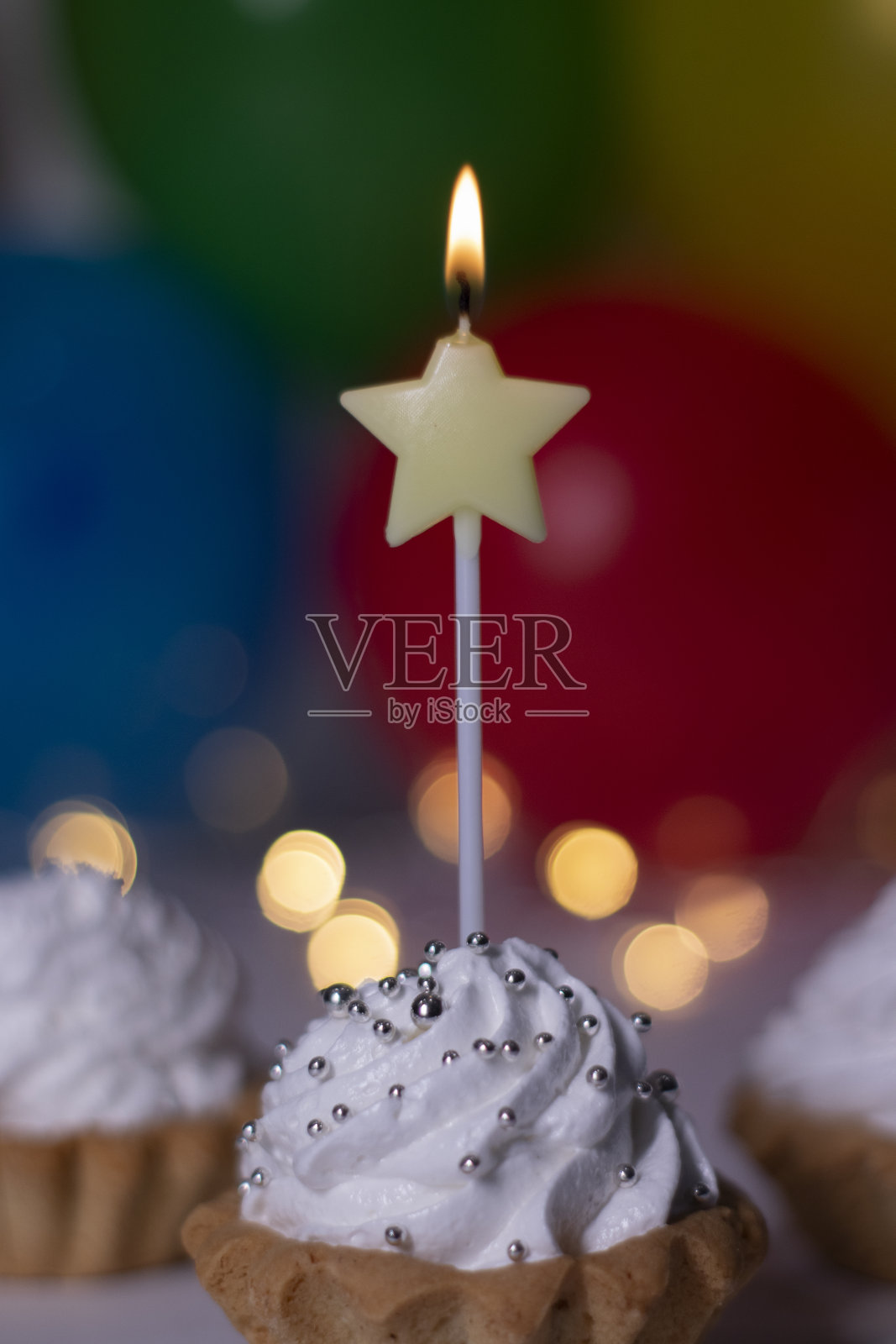 节日纸杯蛋糕配黄色星形蜡烛。背景是五颜六色的气球和灯光。的生日的概念。副本的空间。照片摄影图片