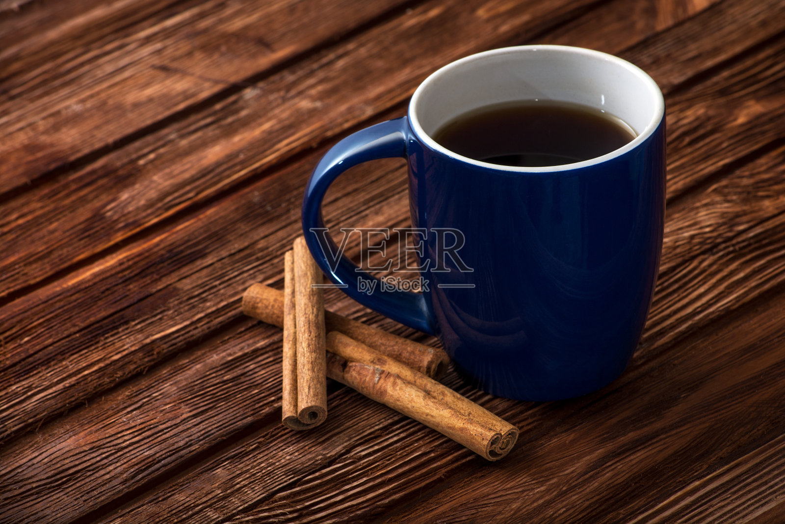 蓝色的茶杯放在一个旧的木头表面上。褐色的旧木板。杯边有肉桂棒和茴芹。家的温馨和舒适的概念。空间的文本。照片摄影图片