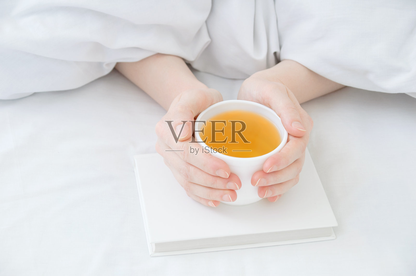 女性的手从毯子下拿着一杯白色的绿茶在她们的手中照片摄影图片