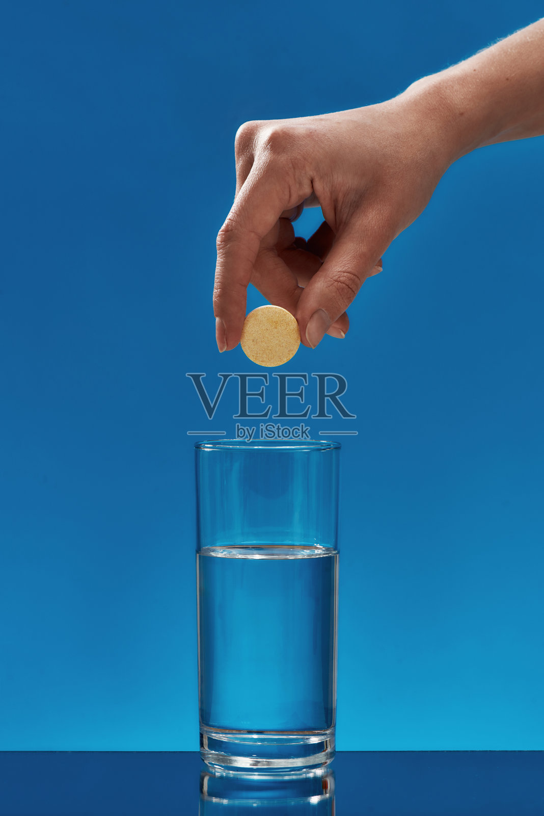 手拿着冒泡的阿司匹林药片,药丸上面的水隔离在蓝色的背景。健康的概念照片摄影图片