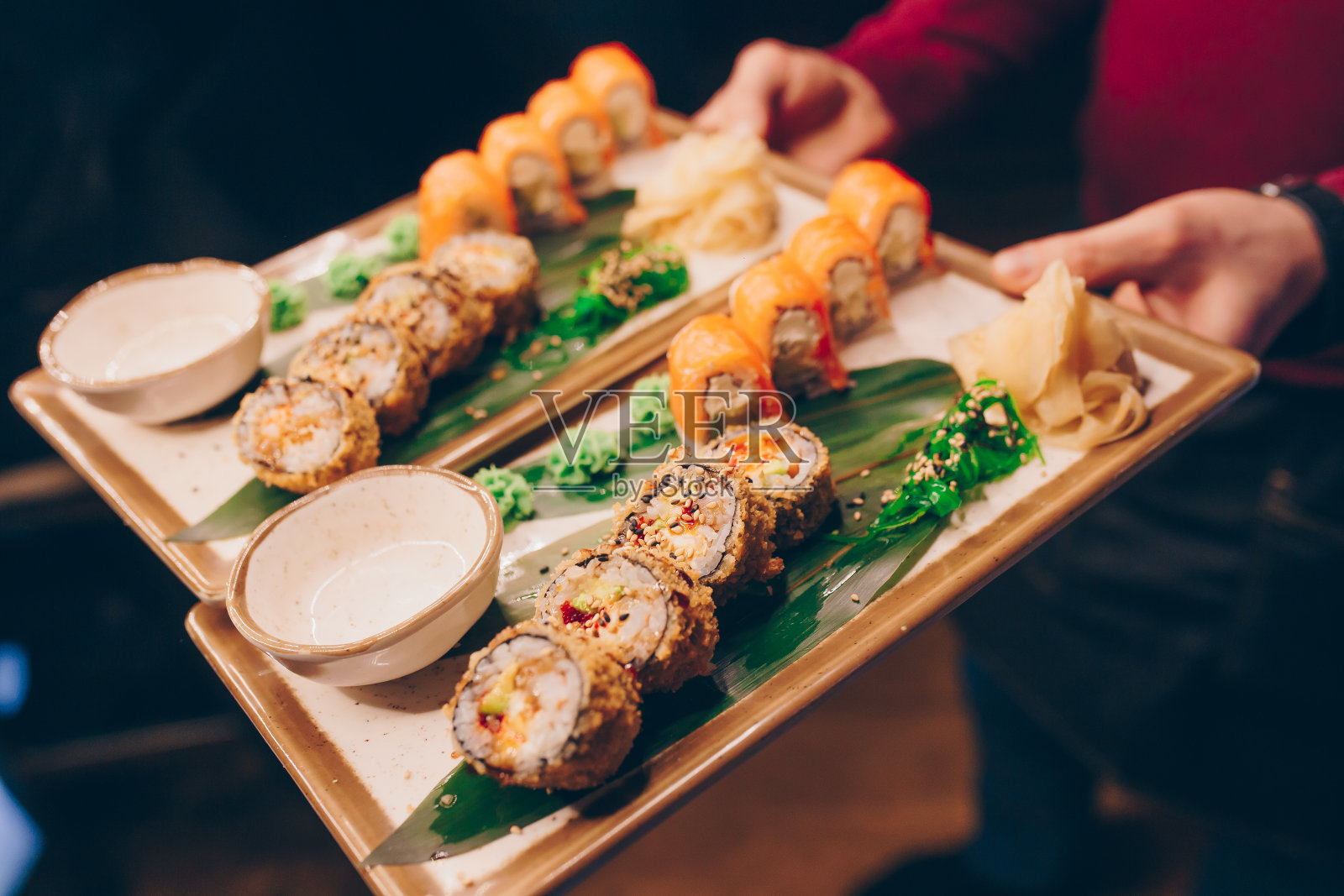 近距离手服务员拿着一套美味新鲜的寿司板寿司卷温热清鳗鱼,日本生鱼片在传统餐厅。寿司吧里的费城肉卷。照片摄影图片