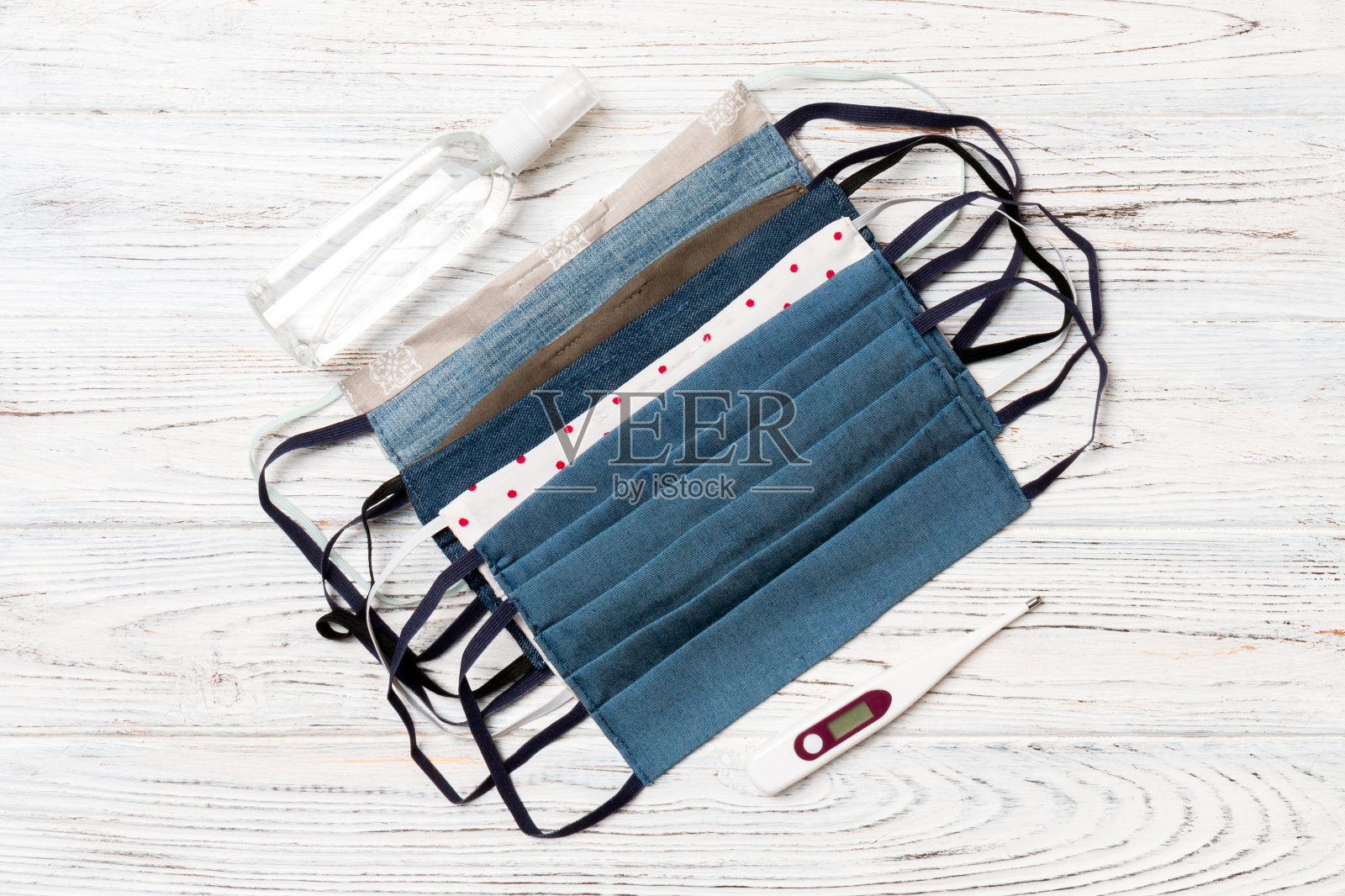 俯视图自制棉口罩,数字温度计和酒精洗手液在木制背景。医疗保健概念与复制空间照片摄影图片