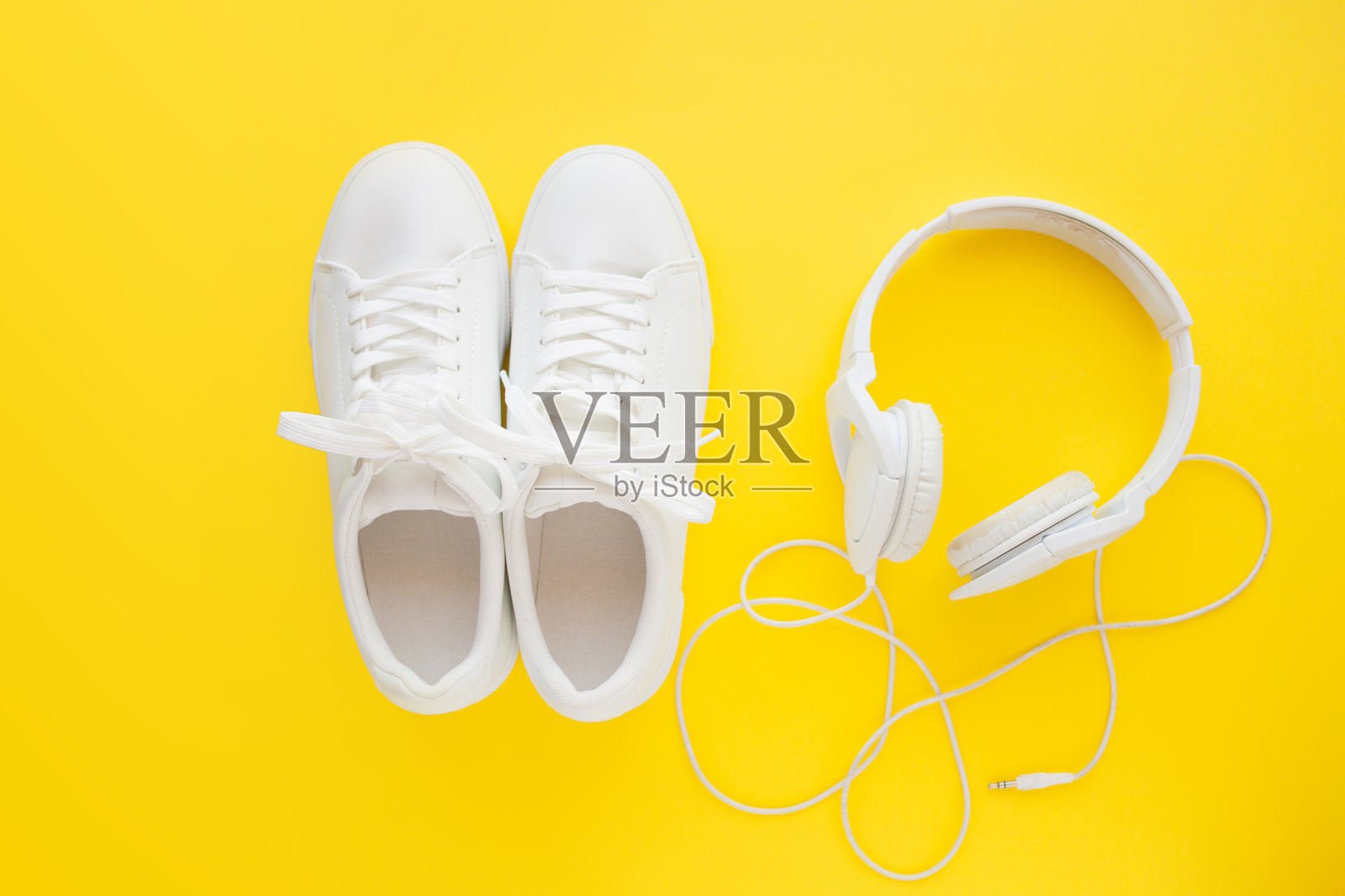 完美的白色新运动鞋站在明亮的黄色背景靠近白色耳机。照片摄影图片