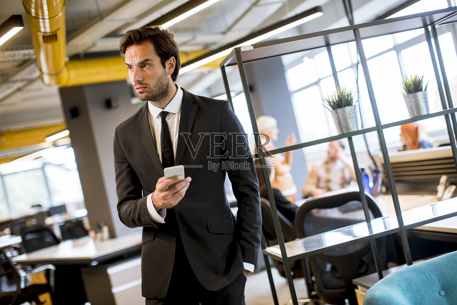 年轻的商人穿着黑色西装在办公室里使用现代智能手机照片摄影图片